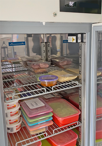 Sensono Sensorbox in einem KITA oder Hort Kühlschrank zur Temperaturüberwachung Die Sencono Temperatur Sensorbox ist auf diesem Bild in einem Kita-Kühlschrank zu sehen. Die Box ist an der oberen rechten Seite des Kühlschranks angebracht und misst die Temperatur im Inneren. Das Gehäuse der Sensorbox ist schwarz und hat eine rechteckige Form. An der Vorderseite der Box befinden sich zwei kleine runde Löcher, die für die Messung der Temperatur genutzt werden. Die Box ist mit einer Kunststoffhalterung befestigt, die an der Wand des Kühlschranks angebracht ist. Der Kita-Kühlschrank selbst hat ein weißes Gehäuse und ist mit Lebensmitteln und Getränken gefüllt.
